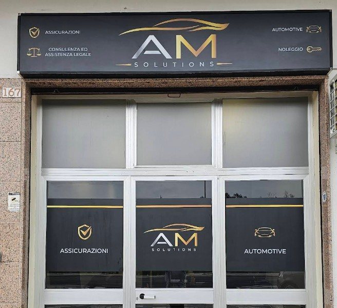 Vetrina di A M Solutions con insegna nera e oro, numero civico 167 e scritte Assicurazioni, Automotive, Noleggio