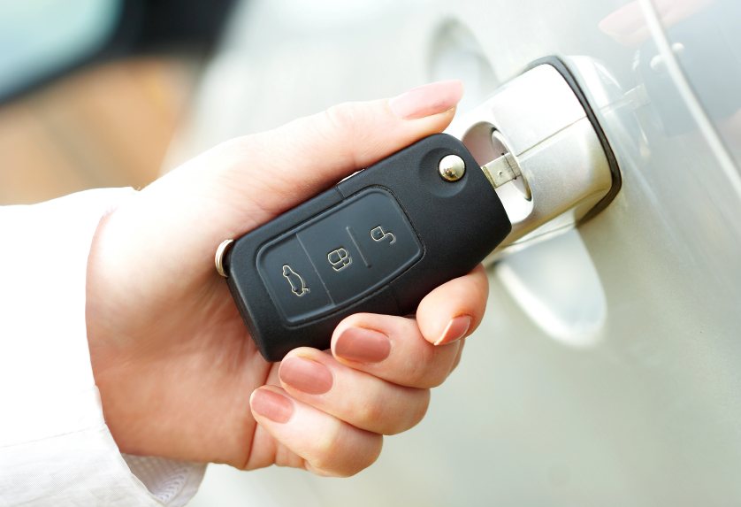 Mano con smalto rosa che inserisce una chiave a scatto nera con telecomando nella serratura di un'auto argentata